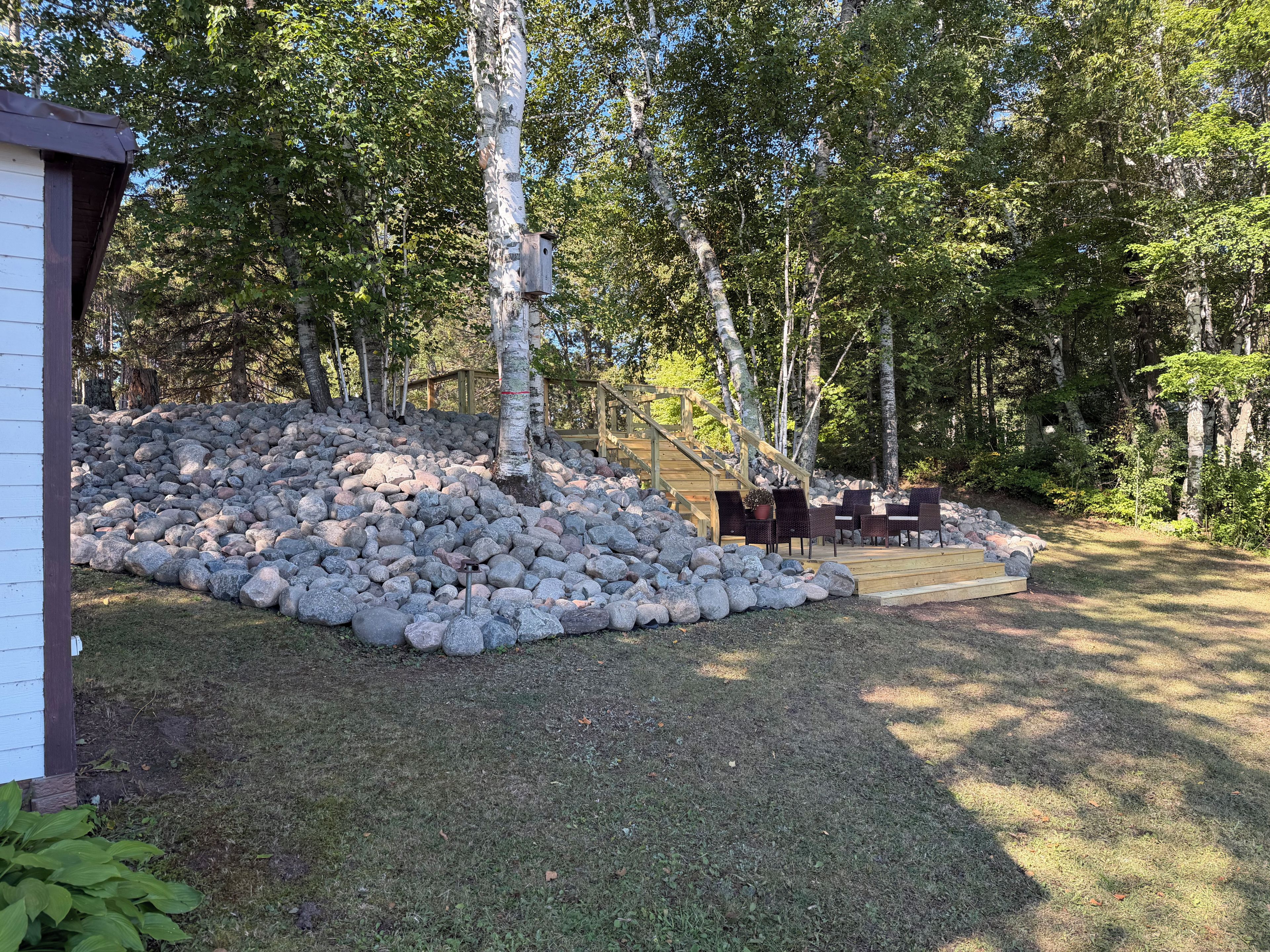 En baghave med en træterrasse, en stenvæg og en trappe til en træterrasse.