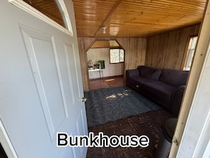A bunkhouse interior with a wooden ceiling, a couch, a door, and a window.
