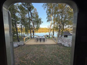 Eine Terrasse mit Tisch und Stühlen mit Blick auf einen See, Bäume und eine Holzhütte.