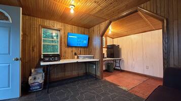 A room with wooden walls, a mounted television, a small table, a trash bin, and a door.