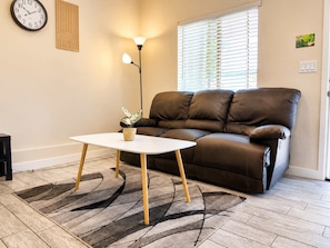 A living room with a brown leather sofa, a white coffee table, a floor lamp, and a wall clock.