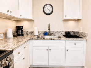 A kitchen with white cabinets, a stainless steel sink, a clock, a coffee maker, and a stove.