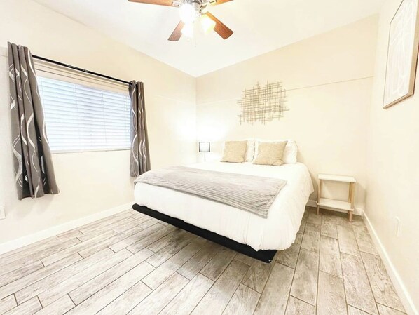 A bedroom with a bed, a ceiling fan, a nightstand, and a window with curtains.