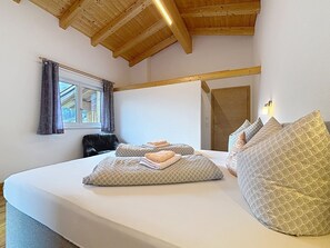 A bedroom with a large bed, wooden ceiling beams, a window with curtains, and a door. - Alpenblick by Interhome (See)