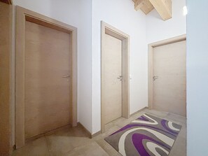 A hallway with three closed doors, a patterned rug on the floor, and a ceiling with exposed wooden beams. - Alpenblick by Interhome (See)