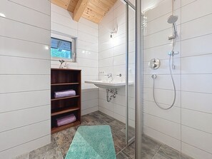A modern bathroom with a glass shower enclosure, a wooden shelf with towels, and a window above the sink. - Alpenblick by Interhome (See)