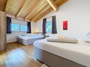 A room with two beds, wooden ceiling beams, a red light switch, and windows with curtains. - Alpenblick by Interhome (See)