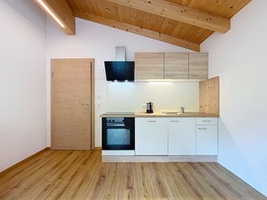 A compact kitchen with wooden flooring, white cabinetry, a black range hood, and a built-in oven. - Alpenblick by Interhome (See)