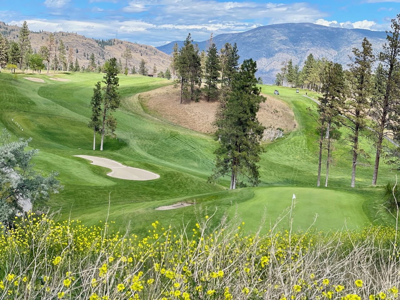 A golf course with a well-maintained fairway, sand bunkers, and a backdrop of mountains.