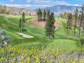 Camp de golf amb un fairway ben cuidat, sorrals i silueta de muntanyes al fons.
