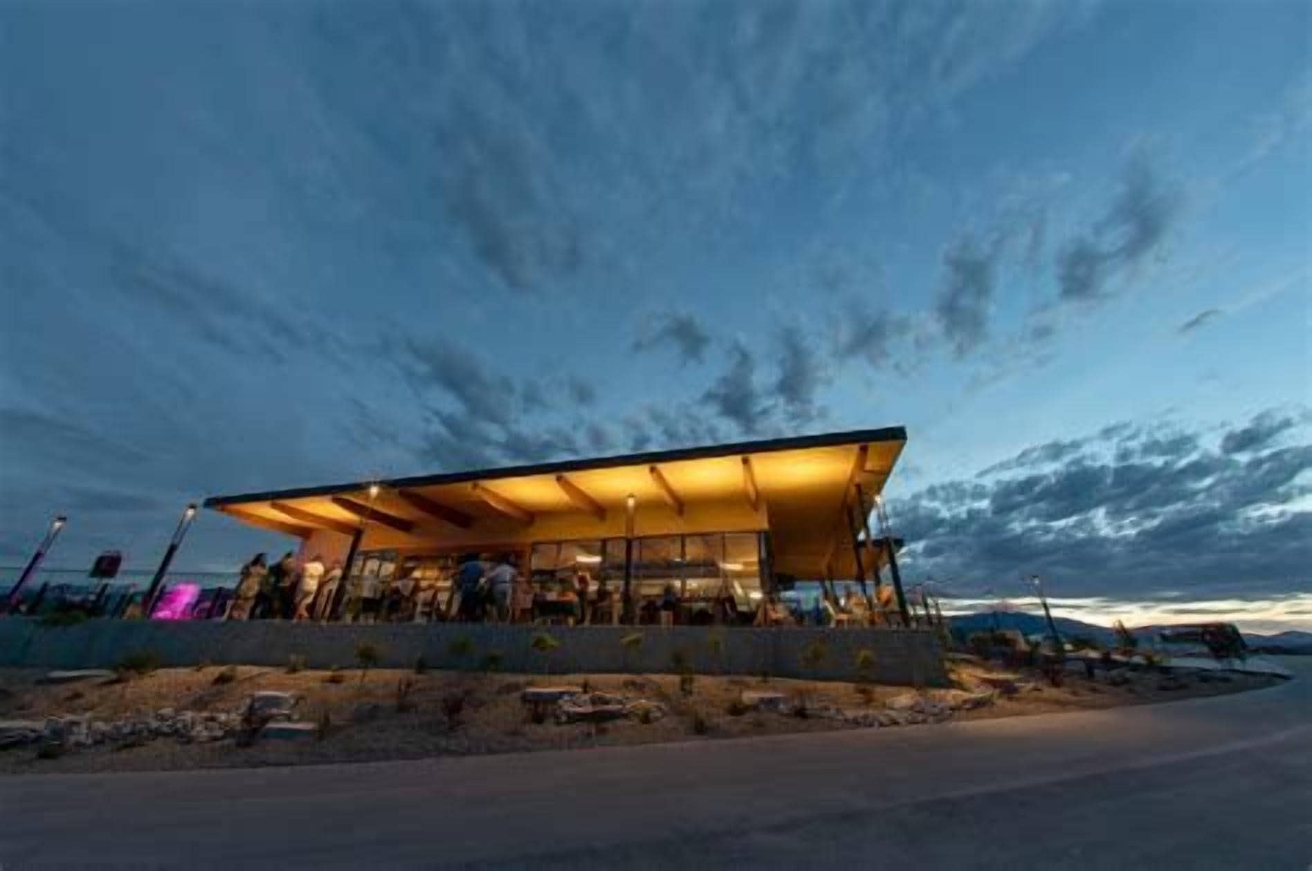 A modern building with a flat roof and a covered outdoor area, possibly a restaurant or cafe, with a clear sky in the background.