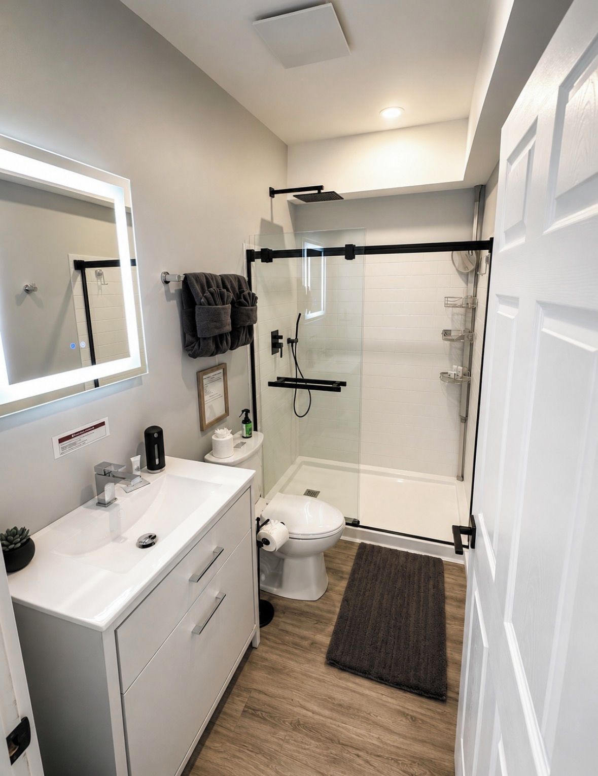 Un baño moderno con ducha envuelta en vidrio, un lavamanos blanco con espejo y un inodoro.