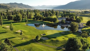 A golf course with a pond, trees, and a distant mountain range.