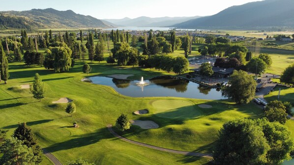 A golf course with a pond, trees, and a distant mountain range.