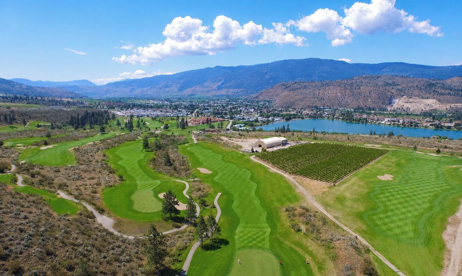 A golf course with multiple greens, a clubhouse, and a lake in the background.