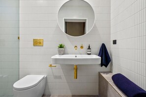 Ein Badezimmer mit weiß gefliester Wand, einem weißen Waschbecken mit Goldarmatur, einer weißen Toilette und einem blauen Handtuch auf einer Ablage.