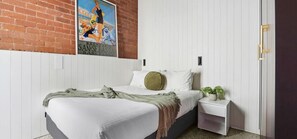 Ein Schlafzimmer mit einem Bett, einem Nachttisch, einer Topfpflanze, einem Poster an der Wand und einer Tür.