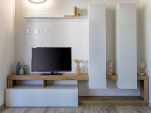 Ein modernes Wohnzimmer mit einem Flachbildfernseher, Holzregalen und einem weißen Konsolentisch.