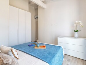 Een slaapkamer met een bed, nachtkastje, dressoir en raam.