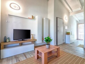 Ein modernes Wohnzimmer mit einem Flachbildfernseher, einer hölzernen Bank, einem Blumentopf und einer Küche im Hintergrund.