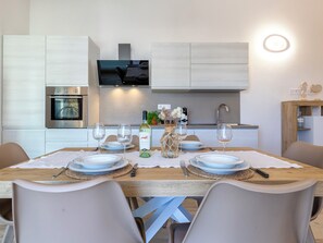 Una cocina moderna con electrodomésticos integrados, una mesa de comedor lista para cuatro personas y un televisor montado sobre la encimera.
