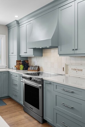 A kitchen with grey cabinets, a stainless steel range, and a white countertop.