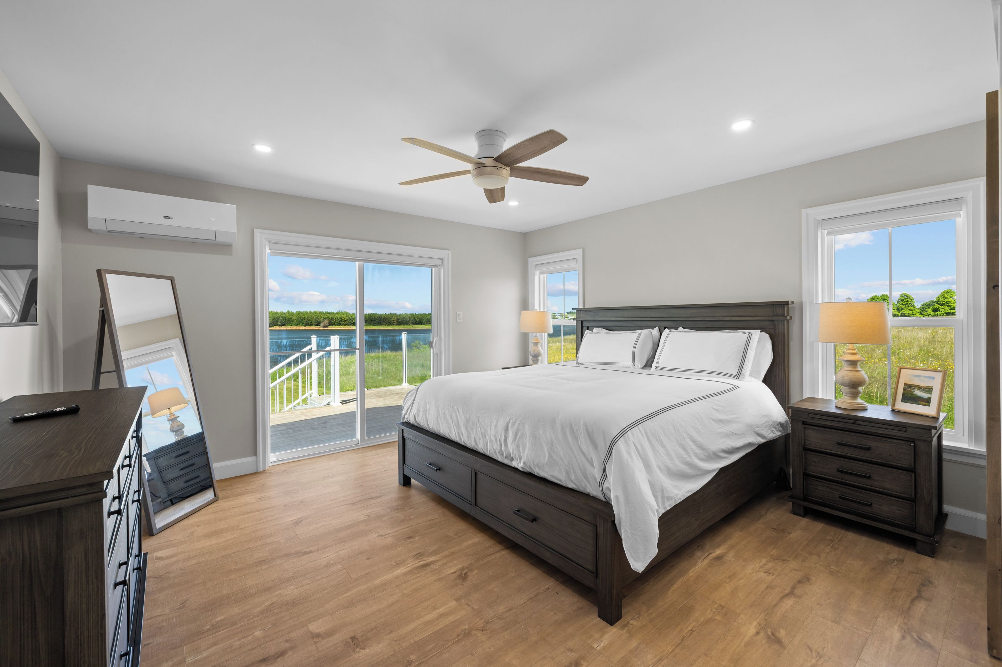 A bedroom with a large bed, a ceiling fan, and a view of a lake through the windows.