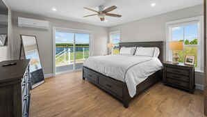 A bedroom with a large bed, a ceiling fan, and a view of a lake through the windows. - Private PEI Waterfront Escape | 5BR | Dock | Beach | Golf & Cavendish Nearby (Kensington)
