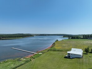 A large body of water with a dock extending into it, surrounded by grassy fields and a single white building.
