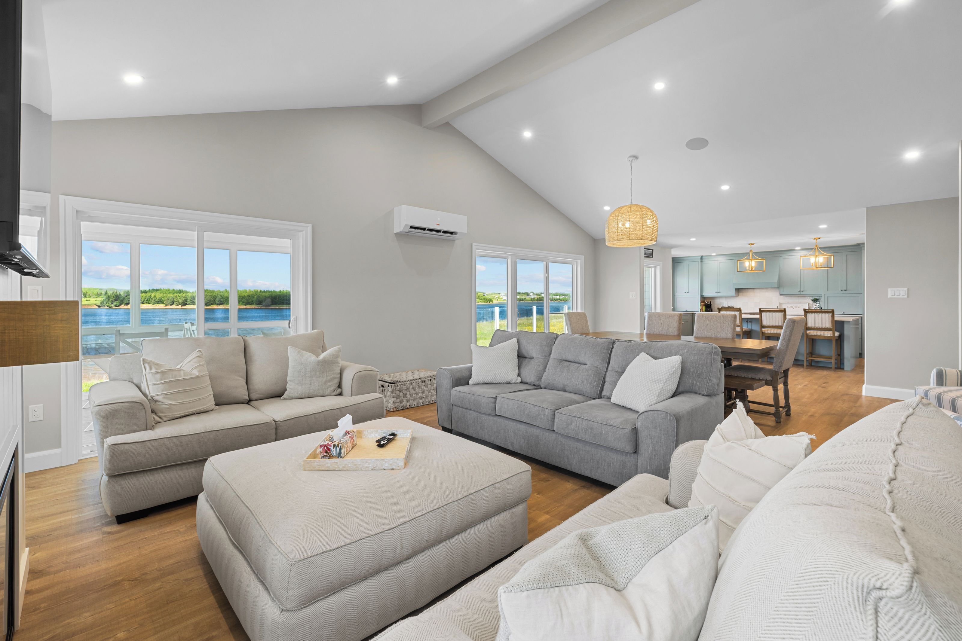 A spacious living room with a large window overlooking a body of water, a dining area with a view, and a kitchen with light blue cabinets.