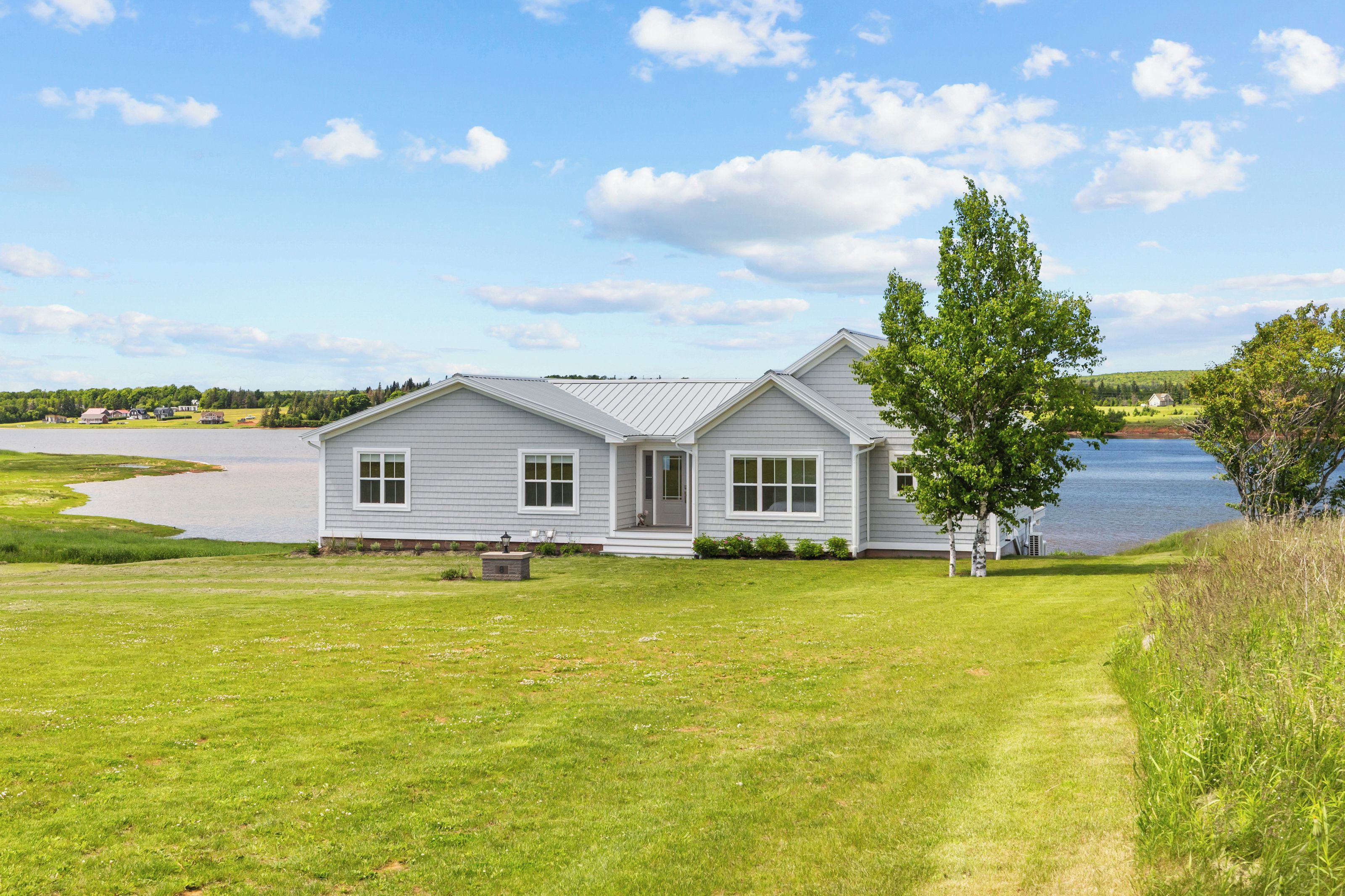 A single-story house with a front porch, a lawn, and a body of water in the background.