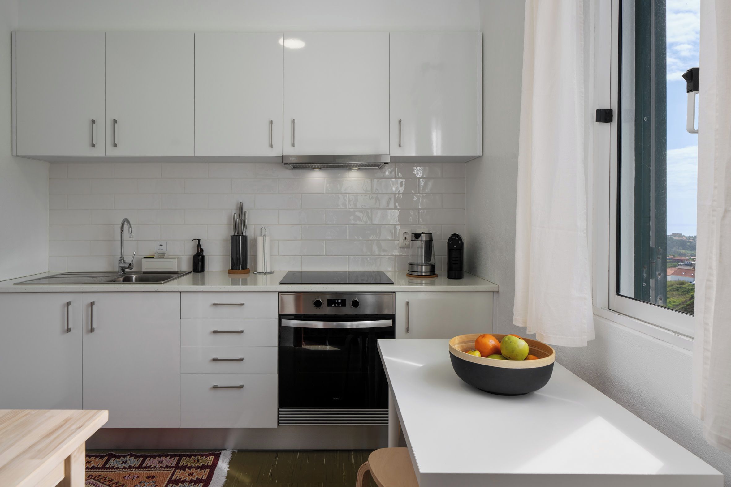 A modern kitchen with white cabinets, a stainless steel oven, and a window with a view.