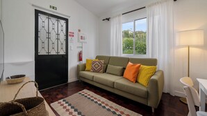 Un salon confortable avec un canapé, un tapis à motifs, une fenêtre avec des rideaux et une porte signalée comme issue de secours.