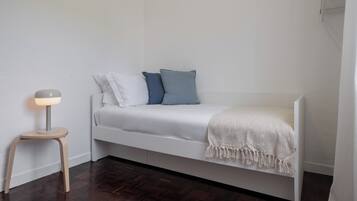 A small, single-bed room with a white bed, a bedside lamp, and a wooden floor.