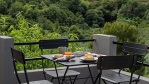 Une table dressée à l’extérieur, avec des chaises, un livre, un verre de jus d’orange, une assiette avec du pain et une tasse.