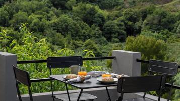 A table set outdoors with chairs, a book, a glass of orange juice, a plate with bread, and a cup.