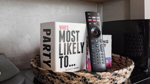 A basket containing a remote control, a book titled 'WHO'S MOST LIKELY TO PARTY', and a sugar container on a shelf. - The A-Frame · Hot Tub, Fire Pit, 30 min to Waco (Valley Mills)