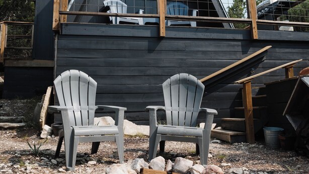 A modern cabin with a triangular roof, wooden deck, and two Adirondack chairs. - The A-Frame · Hot Tub, Fire Pit, 30 min to Waco (Valley Mills)