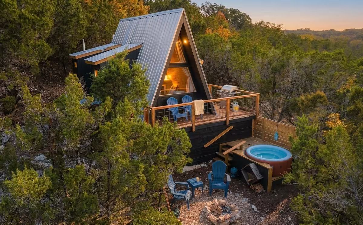 Een chalet met een puntdak, een hottub en een zitgedeelte buiten.