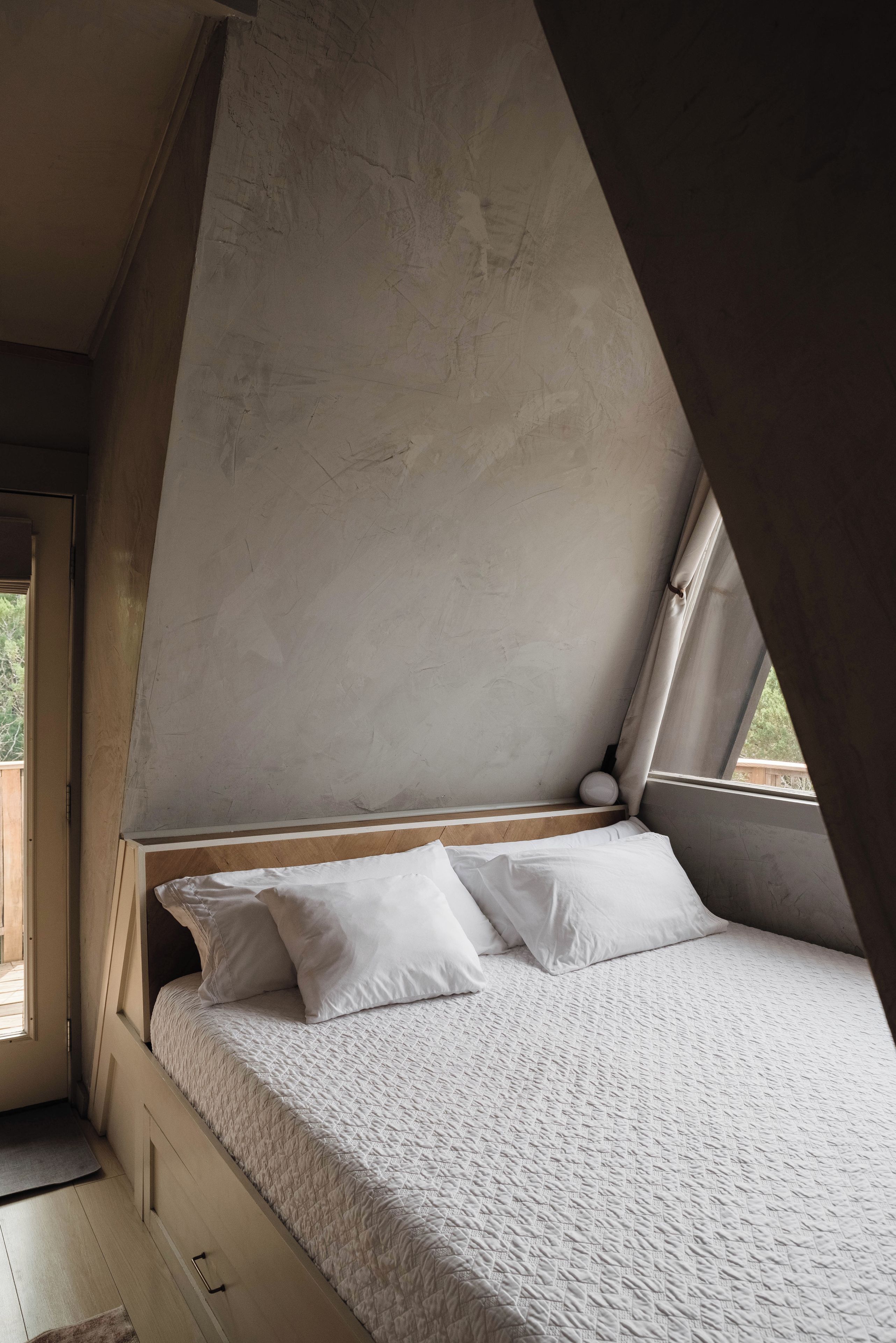 A bedroom with a sloped ceiling, a bed with white bedding, and a window providing natural light.