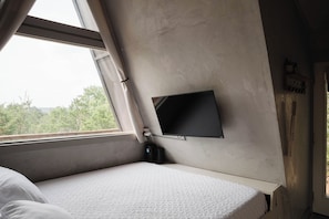Une chambre avec un lit, un téléviseur fixé au mur et une fenêtre avec des rideaux.