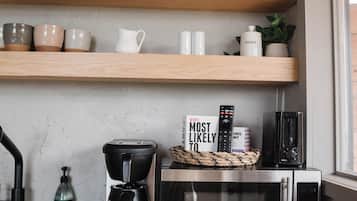 A kitchen with wooden shelves holding dishes, a coffee maker, a microwave, and a sign that says 'Welcome to the A-Family.'