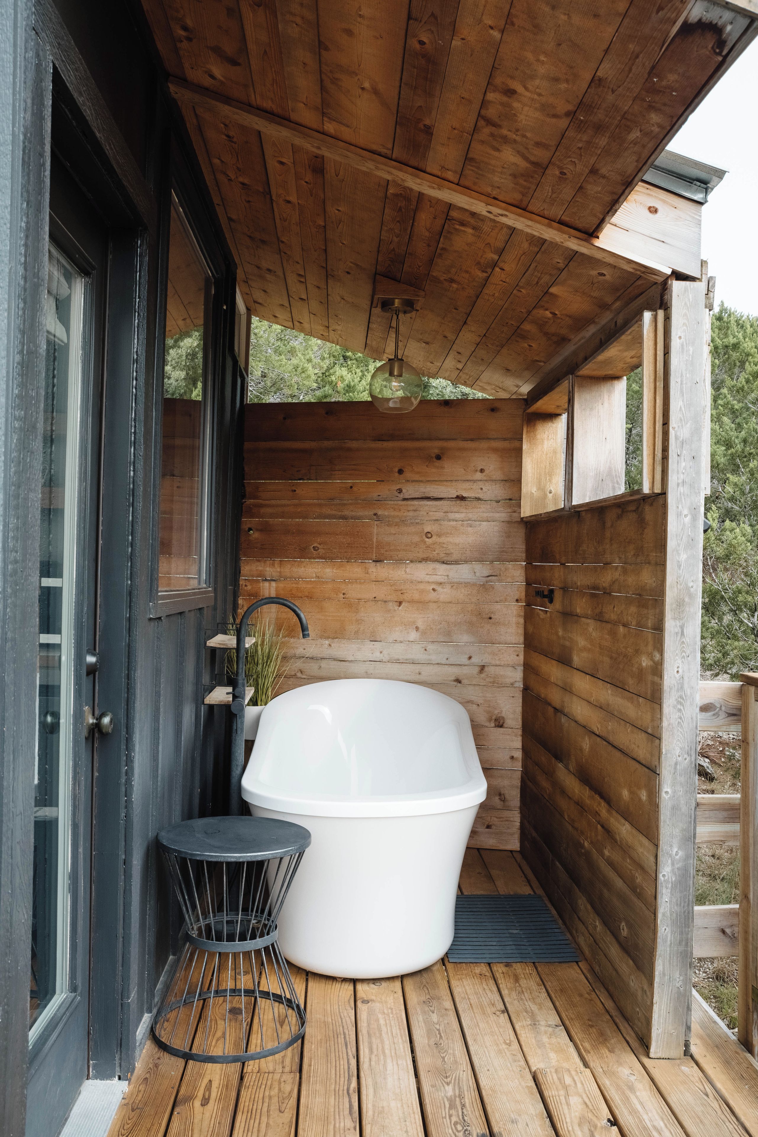 A wooden deck with a white bathtub, a small round table, and a door leading to a covered area.