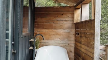 A wooden deck with a white bathtub, a small round table, and a door leading to a covered area.