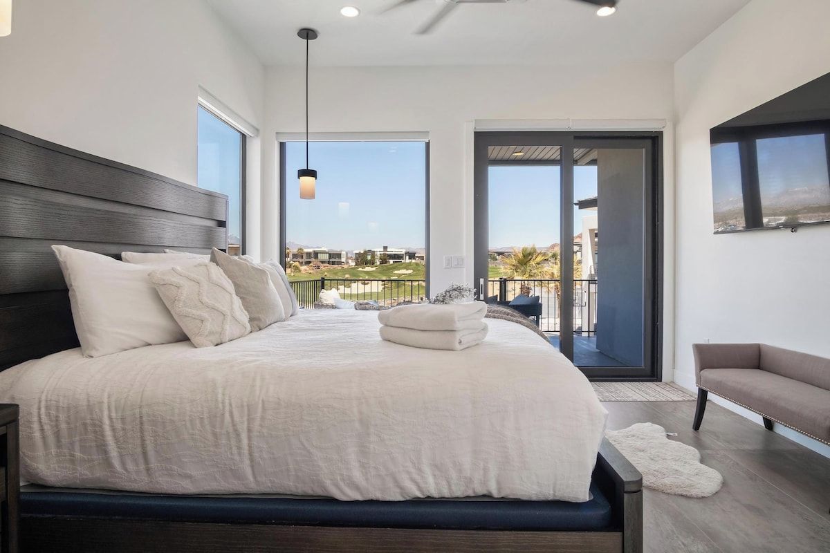 A bedroom with a large bed, a ceiling fan, and a view of a balcony.