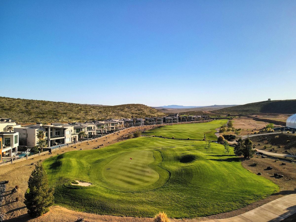 A golf course with a putting green, sand bunkers, and a clubhouse with modern architecture.