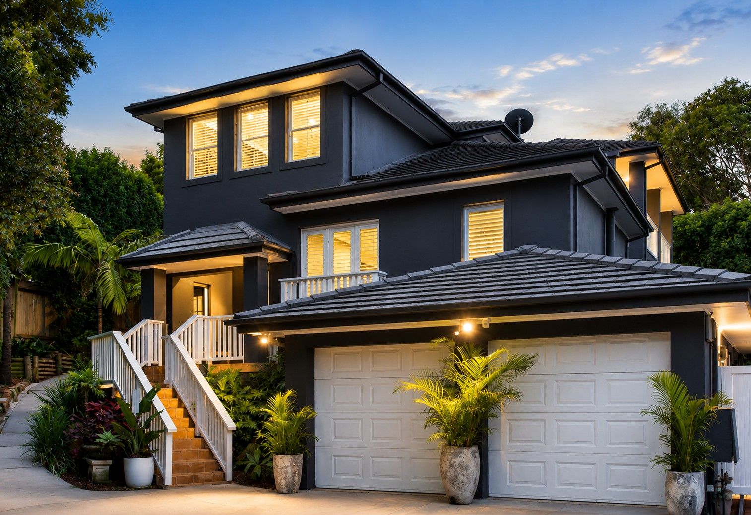 A two-story house with a garage, a staircase, and potted plants.