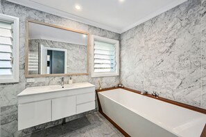 Ein modernes Badezimmer mit Marmorwand, einem großen Spiegel, einer Badewanne und einem Waschtisch.
