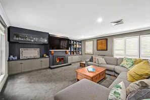 A modern living room with a fireplace, built-in bookshelves, a grey sofa, and a coffee table. - 400 meters to the beach! (Mona Vale)