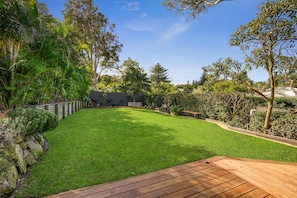 A well-maintained backyard with a wooden deck, a grassy lawn, and various trees and shrubs. - 400 meters to the beach! (Mona Vale)